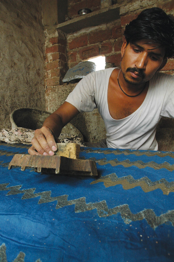 A printer pressing a wooden block onto cloth by hand