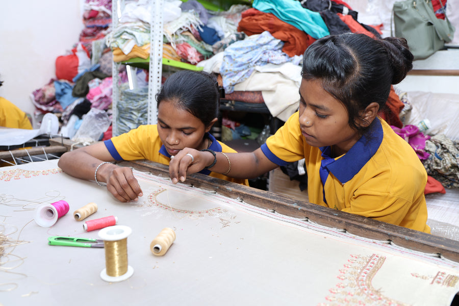 Two young women learning embroidery together at the frame