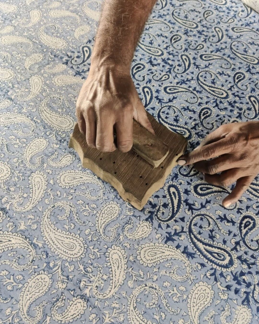 A printer's hands pressing a carved wooden block onto blue and white paisley cloth